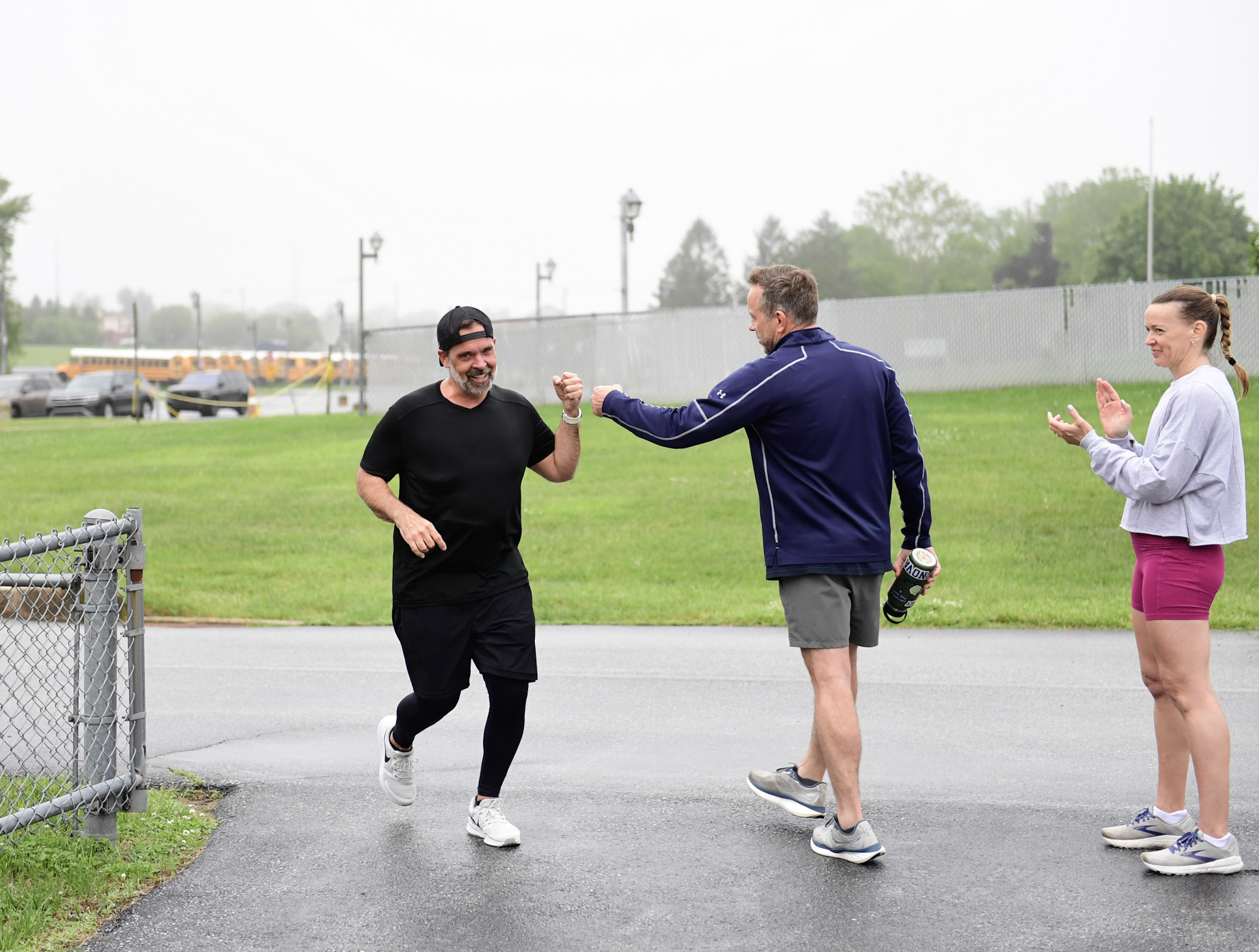 A CrossFit Reckoning member finishing the run portion of Murph 2026 with members cheering and high-fiving in the rain